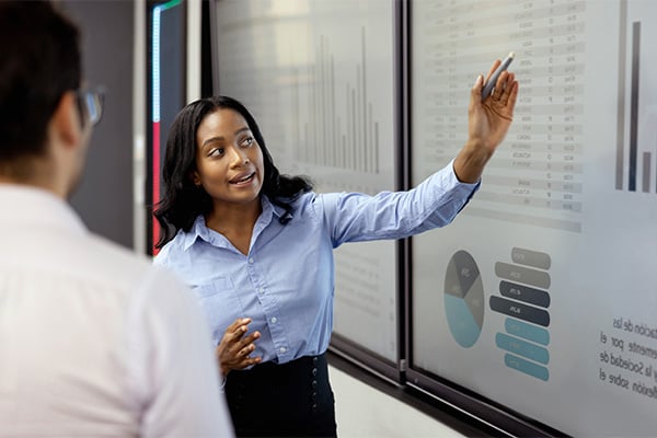 A professional business woman is reviewing statistics on a board with her colleague.